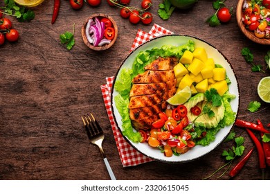 Grilled chicken with side dish salad from avocado, mango, tomato salsa, cilantro, lime and lettuce, rustic wooden table background, top view - Powered by Shutterstock