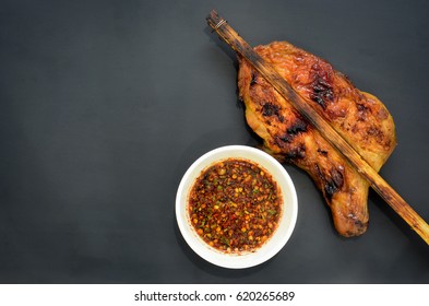 grilled chicken with Thai style dipping spicy sauce for roasted or grilled food (fish sauce and chilli) or Nam Jim Jaew, Thai street food, on black background, copy space