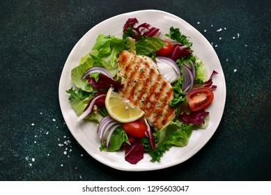 Grilled Chicken Or Turkey Breast With Fresh Vegetable Salad On A White Plate Over Dark Green Slate, Stone Or Concrete Vegetable.Top View With Copy Space.