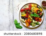 Grilled colorful vegetable : bell pepper, zucchini, eggplant on a plate over light grey slate, stone or concrete background. Top view with copy space.
