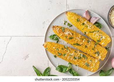 Grilled corn on the cob with butter, parmesan cheese and basil in a plate on stone background. top view with copy space. healthy vegetarian food