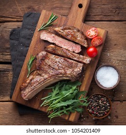 Grilled cowboy beef steak, herbs and spices on a rustic wooden background. Top view - Shutterstock ID 1054201409