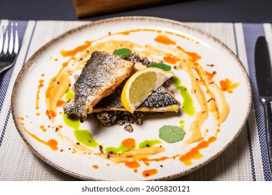 Grilled Dorado fillet on a plate, with sauce and lemon, with fork and knife