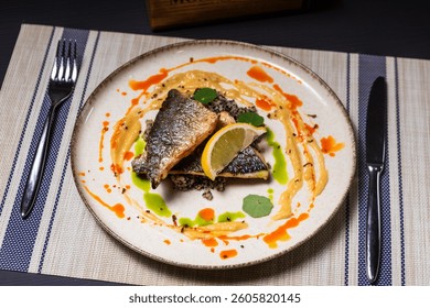 Grilled Dorado fillet on a plate, with sauce and lemon, with fork and knife