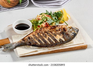 Grilled dorado with garnish on concrete background. Aesthetic composition with bbq fish and vegetables. Healthy food - roasted dorado. Fish dish in minimal style. Whole grilled fish - Shutterstock ID 2158205893