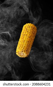 Grilled ear of corn hovering in steam on black background