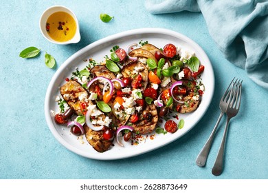 Ensalada de berenjenas a la parrilla con queso feta y tomates en un plato. Fondo azul. Vista superior.