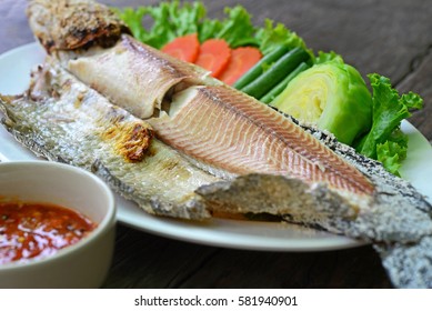 Grilled fillet fish on white plate, serv with fresh vegetables and spicy sauce on the wooden table. (Thai Foods)