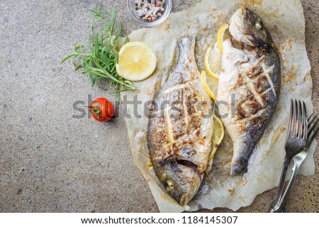 Grilled fish Dorado on paper with lemon and rosemary on gray background, top view