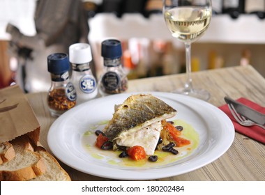 Grilled Fish And Garnitures In Plate And White Wine On Wooden Table