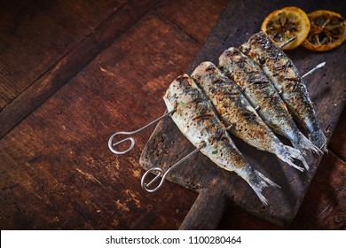 Grilled Fish On Skewers Served On Rustic Wooden Table Viewed In Close-up From Above With Copy Space