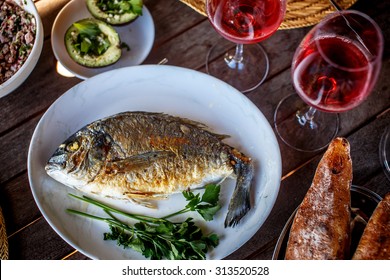 Grilled Fish On White Plate And Wine Glasses.