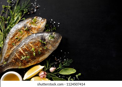 Grilled Fish, Sea Bream With Additions, Herbs, Olive Oil, Spices On A Black Background. Composition In The Bottom Left Corner. Healthy Eating Concept