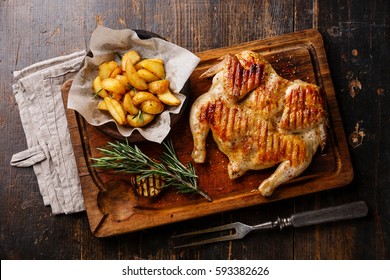 Grilled fried roast Chicken Tabaka and Potato wedges on cutting board on wooden background - Powered by Shutterstock