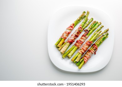 Grilled green asparagus wrapped with bacon. Asparagus baked with bacon and spices. Healthy food. Top view. Free space for your text. Bacon wrapped asparagus on white plate. - Powered by Shutterstock