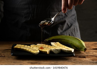 Grilled green banana platan cooked sweet dessert and served with sugar powder and caramel sauce.