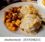 grilled homemade biscuit topped with two sausage patties two scrambled eggs bacon cheddar cheese and sausage gravy served with home fries