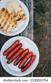 Grilled Hot Dogs And Buns On White Paper Plates On Picnic Table Above Grass. Top Down. Copy Space. 