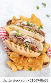 Grilled Hot Dogs With Mustard, Onion, Relish And Corn Chips On A Picnic Table