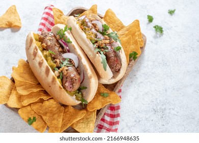 Grilled Hot Dogs With Mustard, Onion, Relish And Corn Chips On A Picnic Table