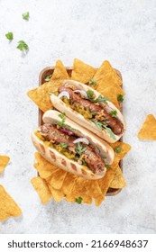 Grilled Hot Dogs With Mustard, Onion, Relish And Corn Chips On A Picnic Table