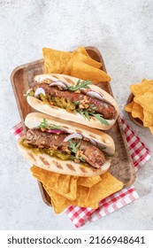 Grilled Hot Dogs With Mustard, Onion, Relish And Corn Chips On A Picnic Table