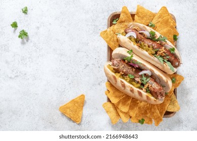 Grilled Hot Dogs With Mustard, Onion, Relish And Corn Chips On A Picnic Table