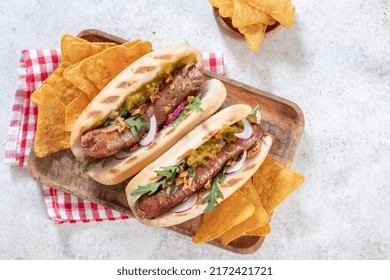 Grilled Hot Dogs With Mustard, Onion, Relish And Corn Chips On A Picnic Table