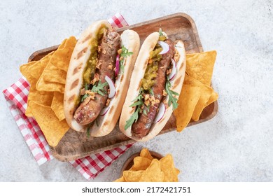 Grilled Hot Dogs With Mustard, Onion, Relish And Corn Chips On A Picnic Table