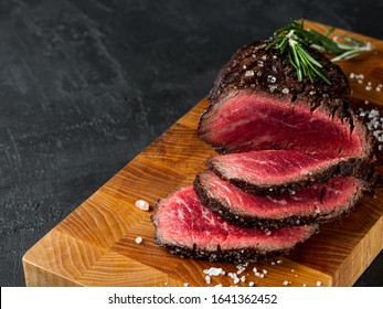 Grilled juicy beef steak selected marbled meat cutting on slices on wooden desk black background with folk and knife.