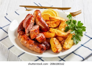 grilled lamb bangers with potatoes and parsley on a white plate on a wooden table, horizontal view from above, close-up