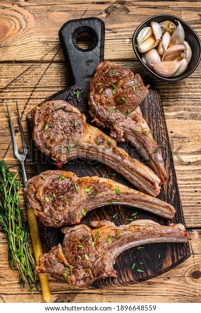 Grilled lamb mutton meat chops\
steaks on a cutting board. wooden background. Top\
view.