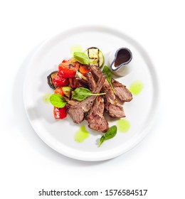 Grilled lamb rack with baked vegetables on white restaurant plate isolated. Delicious fried mutton ribs, roasted cutlets with barbecue pepper, greens and spices top view - Powered by Shutterstock