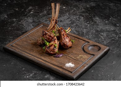 Grilled lamb ribs on cutting board. Hot rack of lamb with spices and condiments. Top view on wooden table
