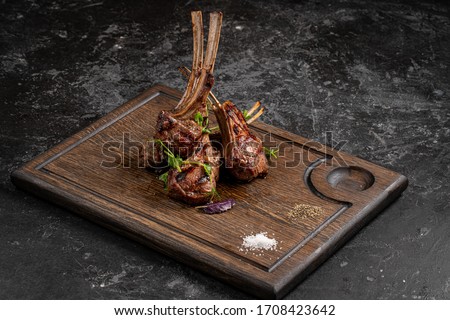 Grilled lamb ribs on cutting board. Hot rack of lamb with spices and condiments. Top view on wooden table