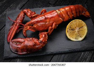 grilled lobster with lemon on a black slate board. on a dark wooden table
