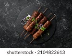 Grilled Lula kebab on skewers with spices in a black plate. On a concrete old table. Top view.