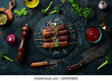 Grilled Lula kebab on skewers with spices in a black plate. On a concrete old table. Top view.