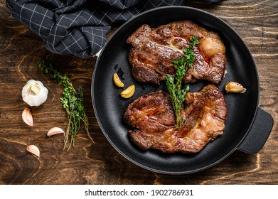 Grilled marble meat steaks Chuck eye roll in a pan. Dark wooden background. Top view.