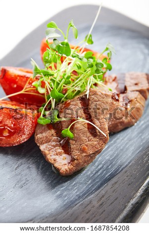 Grilled marbled beef with tomatoes closeup view. Roasted meat with cut vegetables and garden cress. Tasty dish served with greenery and sauce on wooden surface. Haute cuisine, restaurant food