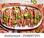 Grilled marinated Angus flank steak, sliced and served on an oval tray sprinkled with sliced jalapenos, chimichurri sauce, and flaky salt, top view