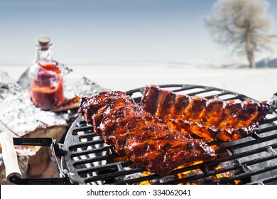 Grilled marinated spare ribs cooking over the hot coals on a barbecue outdoors in a snowy winter landscape