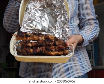 Grilled Meat In Disposable Packaging And Aluminum Foil From The Restaurant. Home Delivery From Restaurants And Cafes. Female Hands In Disposable Gloves Hold Meat On A Stick