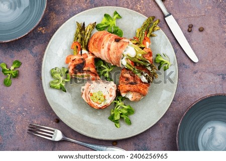 Grilled meat rolls wrapped in bacon with green young asparagus on a plate. Top view.