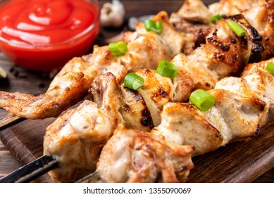 Grilled meat skewers, shish kebab with ketchup and spices on dark wooden background. Chicken shashlik.