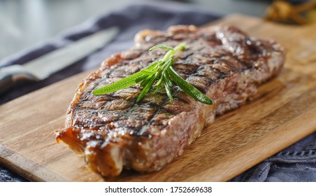 Grilled New York Strip Steak Resting On Wooden Cutting Board With Rosemary Garnish