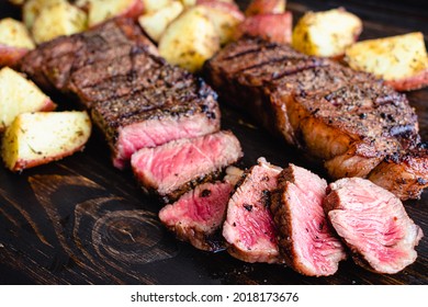 Grilled NY Strip Steak with Coffee Rub and Roasted Potatoes: Grilled New York strip steaks with roasted potatoes on a dark wood background - Shutterstock ID 2018173676