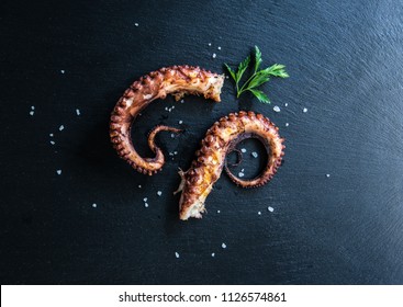 Grilled Octopus appetizer food concept image on black stone table from top view. Seafood meal presentation on black background. Grilled Octopus with salt and herb