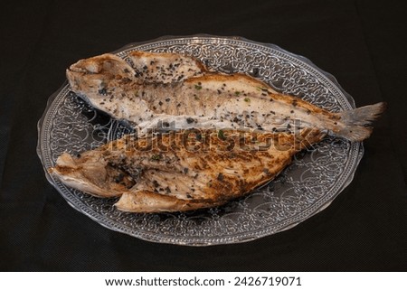 Grilled opened gilt-head bream on glass plate with parsley