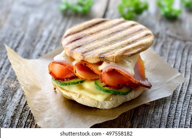 Grilled panini with ham, cheese and cucmber served on sandwich paper on a wooden table